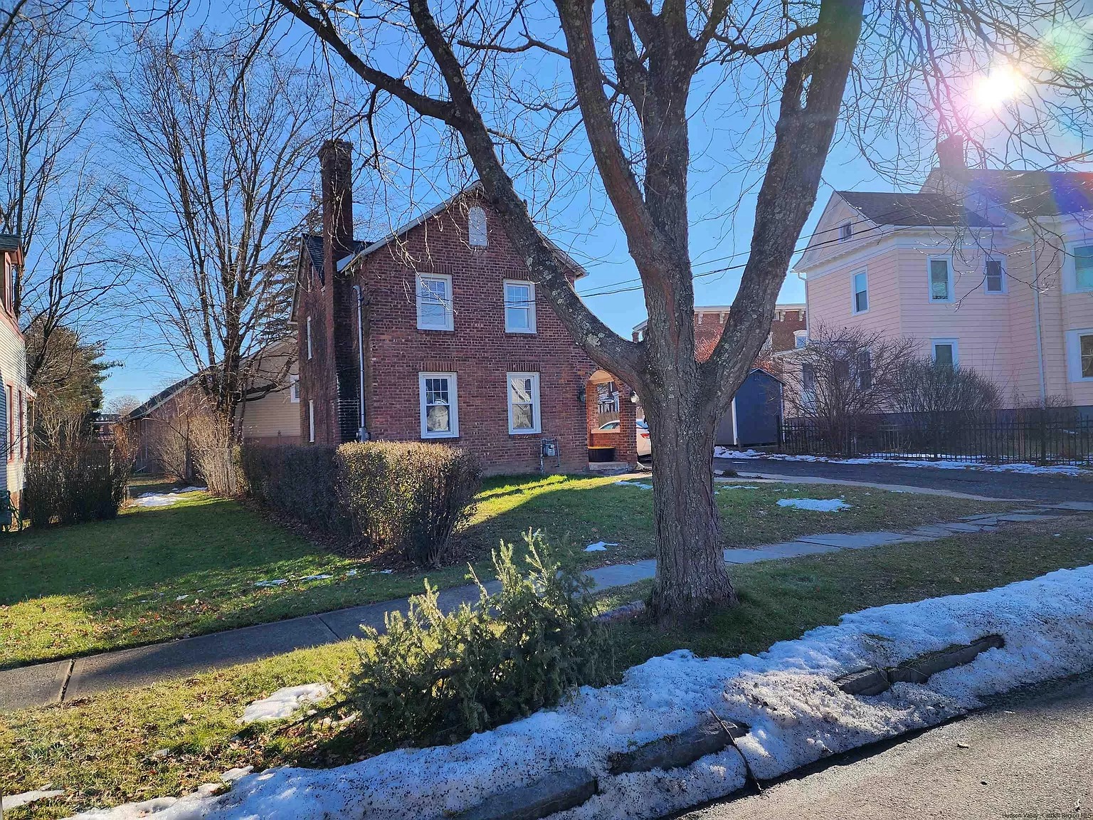 Residential front yard of brick two-story in Saugerties with sidewalk and snowdrift